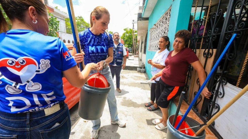 Volunteers in blue shirts with a heart logo hand out supplies on a sunny sidewalk buckets and cleaning tools nearby as residents watch   Informe Regio