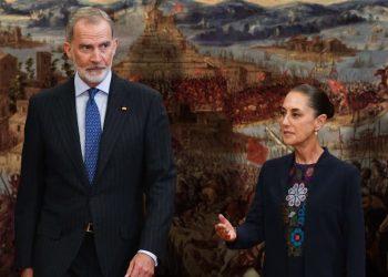 Two formally dressed individuals stand before a large mural of a historic battle scene   Informe Regio