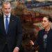 Two formally dressed individuals stand before a large mural of a historic battle scene   Informe Regio
