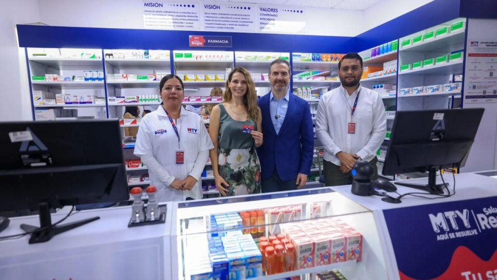 Four people stand behind a pharmacy counter inside a bright drugstore smiling at the camera Two are staff in white coats one man in a blue suit and a woman in a floral dress with shelves of medicines in the background   Informe Regio