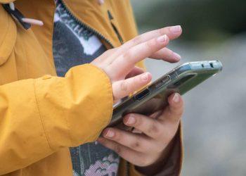 Person in a mustard yellow jacket taps the screen of a smartphone outdoors showing hands and device   Informe Regio