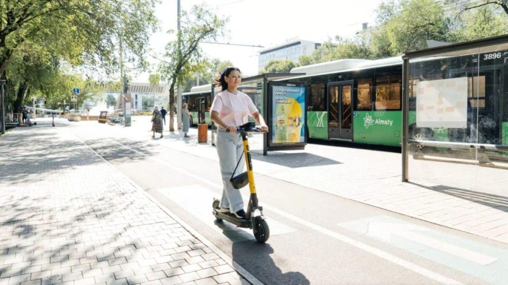 Woman rides a yellow electric scooter on a sunny city sidewalk with a green tram in the background   Informe Regio