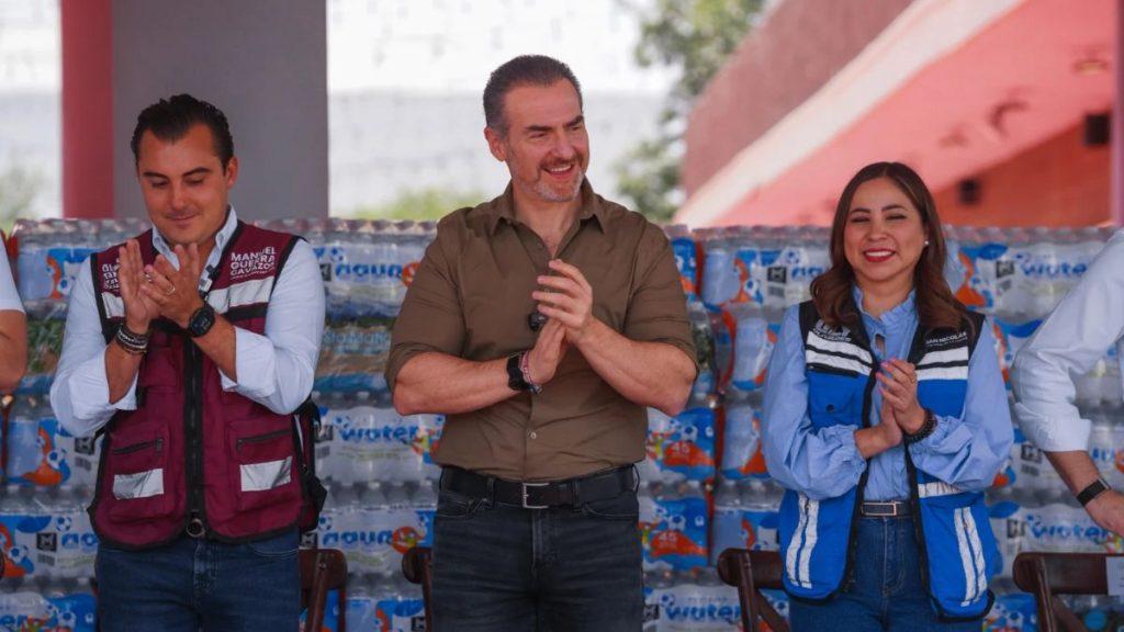 Three adults stand side by side clapping with stacks of bottled water in the background   Informe Regio
