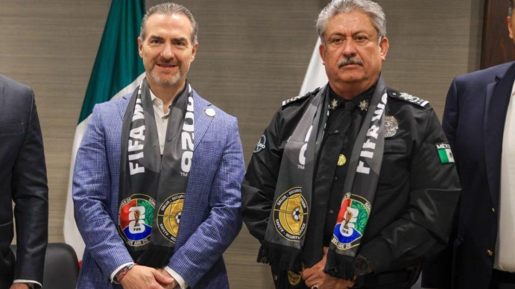 Adrian-de-la-garza 2 - Informe Regio Two men pose for a photo wearing FIFA scarves left man in a blue suit right man in a police uniform indoors with a flag in the background Informe Regio