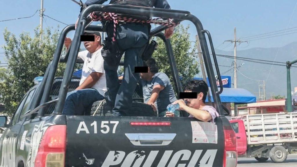 Police pickup with detainees on the back some standing and others seated inside a roll cage black bars over eyes for anonymity a man drinks water at the edge of the tailgate   Informe Regio