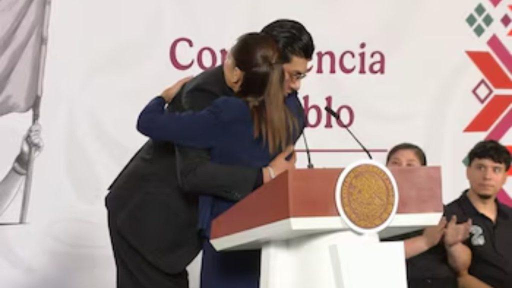 Claudia-sheinbaum-bogueto-mañanera - Informe Regio Two people hug at a podium during a formal event with microphones and a banner in the background Informe Regio