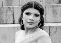 Portrait of a woman with dark hair in an off shoulder gown wearing statement earrings posed on concrete steps in black and white   Informe Regio