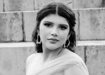 Portrait of a woman with dark hair in an off shoulder gown wearing statement earrings posed on concrete steps in black and white   Informe Regio