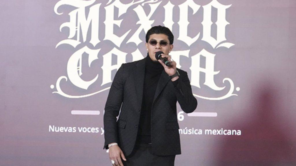 El-bogueto-mañanera-regetton - Informe Regio Male singer in a black suit performing on stage with a handheld microphone backdrop features large white MEXICO lettering Informe Regio