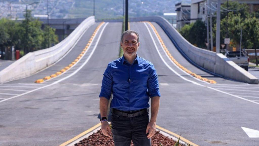 Man in a blue shirt stands on a paved road with a long curved bridge ramp behind him on a sunny day   Informe Regio