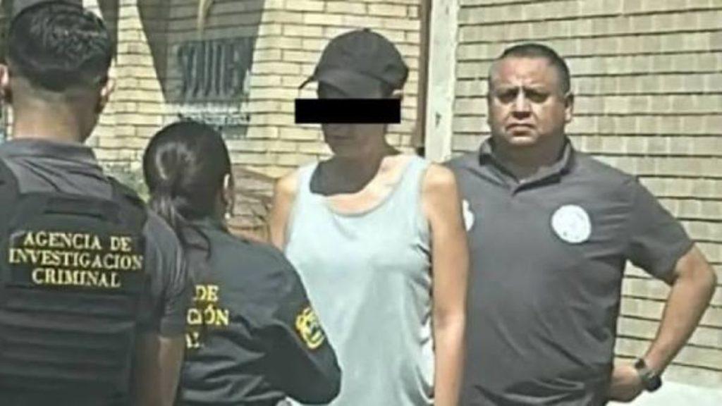 Suspect in a light gray tank top with eyes blacked out stands between two investigators in dark uniforms outside a brick building   Informe Regio