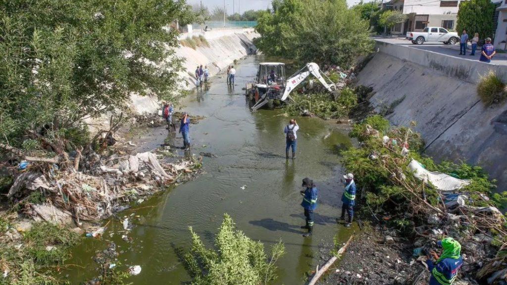 Limpieza-canal-aztlan - Informe Regio Workers in a polluted canal using heavy machinery to remove debris and trash along a concrete canal bank Informe Regio