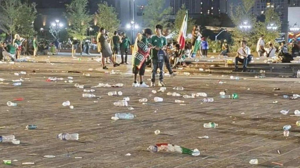 Macroplaza-partidos-limpian-macroplaza-monterrey - Informe Regio Nighttime public square littered with plastic bottles as people mingle in the background one group holding a flag in the center Informe Regio