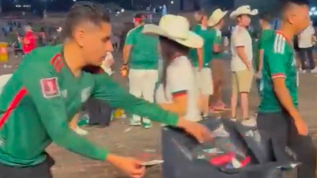 Mundial-méxico-inglaterra-macroplaza-limpieza - Informe Regio Young man in a green sports jersey puts trash into a large trash bin at a crowded outdoor event or stadium area at duskevening Informe Regio