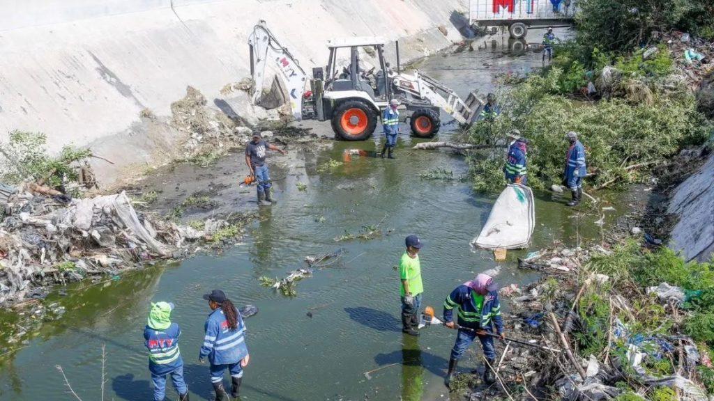 Operativos-limpieza-arroyos-monterrey - Informe Regio Workers in reflective gear wade in a polluted river as a backhoe clears debris during a cleanup operation Informe Regio