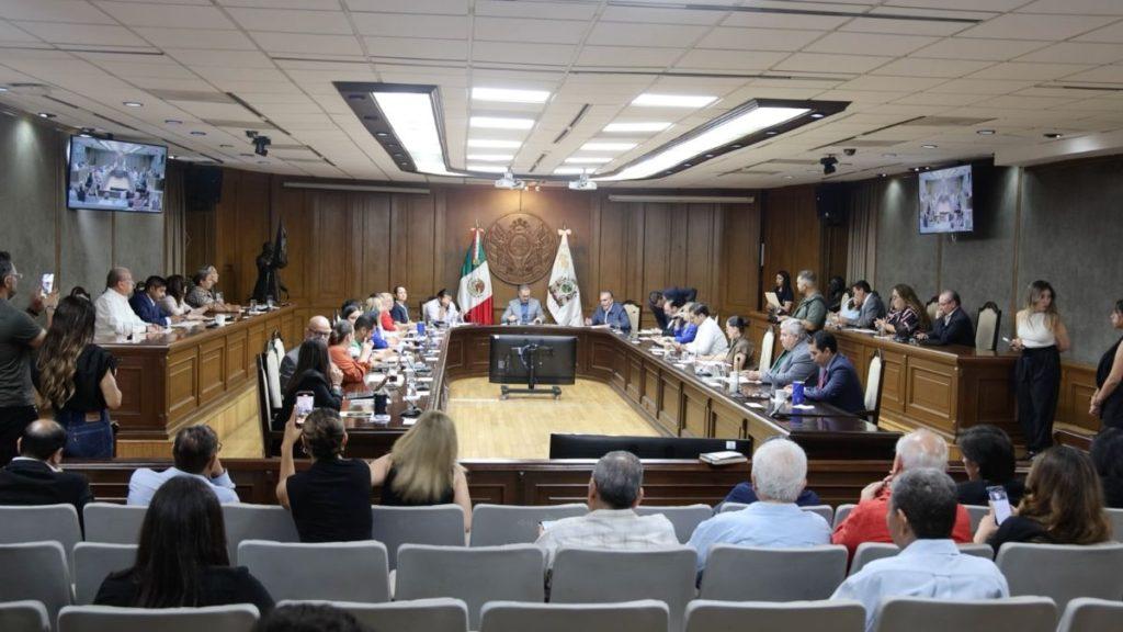 Officials seated around a U shaped conference table in a government chamber with flags in the background   Informe Regio