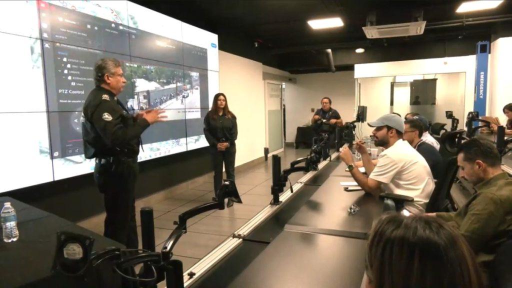 Police officer giving a briefing to journalists in a modern briefing room with a large screen wall and a female assistant standing nearby   Informe Regio