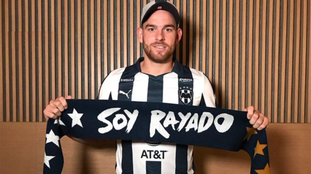 Man wearing a black and white striped soccer jersey holds a navy scarf that reads Soy Rayado with stars at the ends in front of wood paneling   Informe Regio