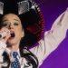 Performer wearing a large decorative sombrero singing into a microphone with one arm raised on a purple lit stage   Informe Regio