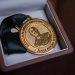 Gold medal resting in a wooden presentation box with a black ribbon attached to it   Informe Regio