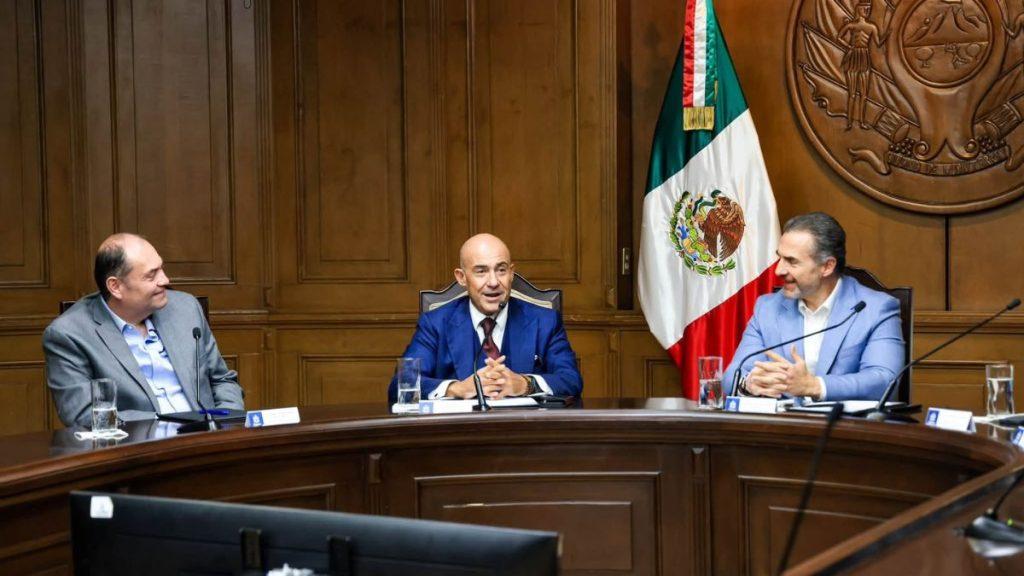 Administracion-adrian-de-la-garza - Informe Regio Three men in suits sit at a curved wood conference table Mexican flag and seal on the wall behind them Informe Regio