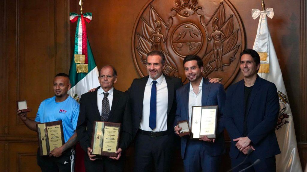 Five men in suits and athletic wear pose with awards in a wood paneled room a Mexican flag visible on the left and a large seal behind them   Informe Regio