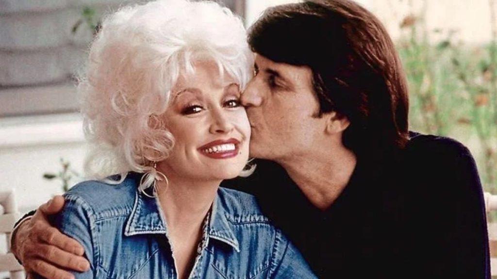 Dolly-parton-esposo-carl-dean - Informe Regio Older woman with white hair smiling as a man kisses her cheek arms around her shoulders denim jacket visible in a casual outdoor setting Informe Regio