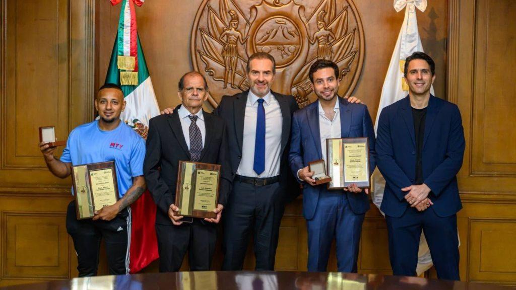 Five men in a formal awards ceremony pose with plaques and medals standing in front of a carved wooden seal and flags   Informe Regio