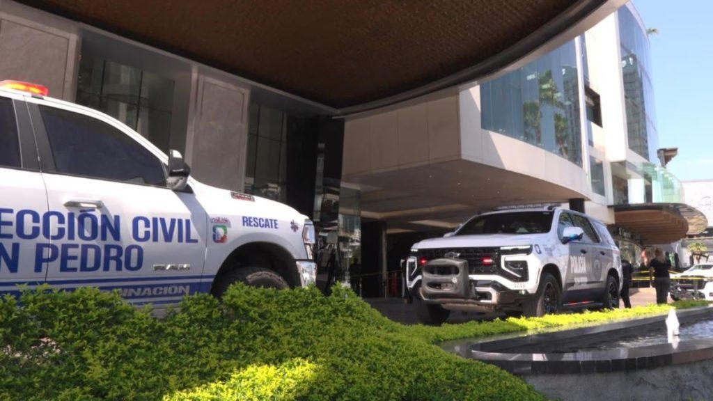 Feminicidio-hotel-safi-personas - Informe Regio Emergency vehicles including a white police SUV with a front grille guard and a rescue van parked outside a modern glass front building with landscaped shrubs in the foreground Informe Regio