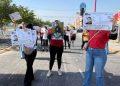 Group of people marching on a street holding large missing person or identification flyers sunny day storefronts visible in background   Informe Regio