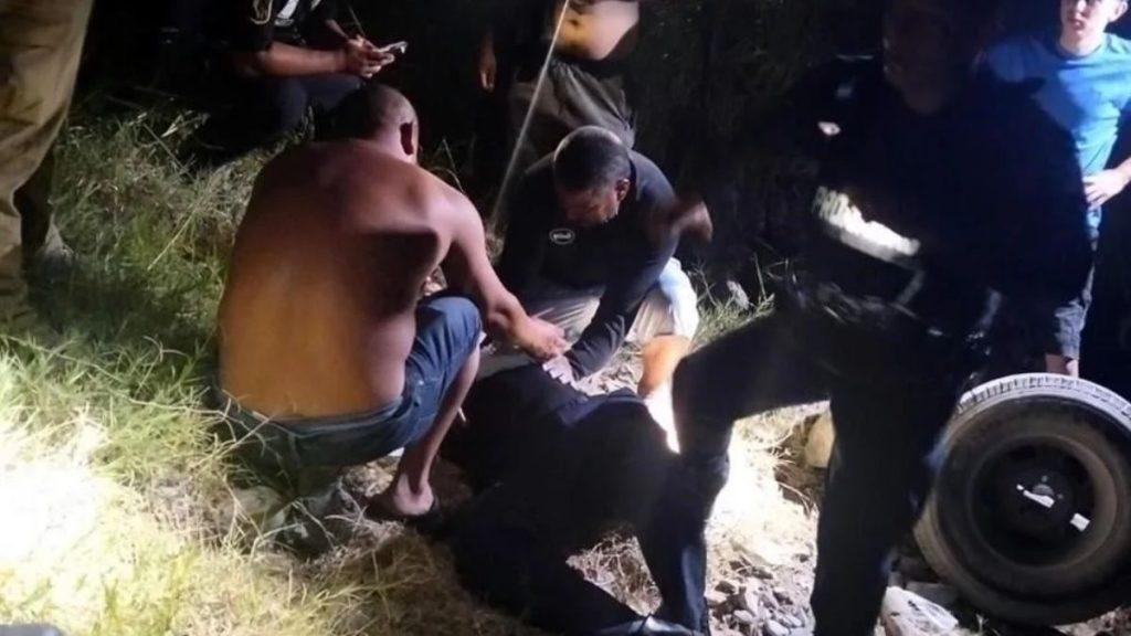 Nighttime outdoor rescue scene several men surround a person lying on the ground while others watch a shirtless man kneels nearby and a police officer stands with a tire in the scene   Informe Regio
