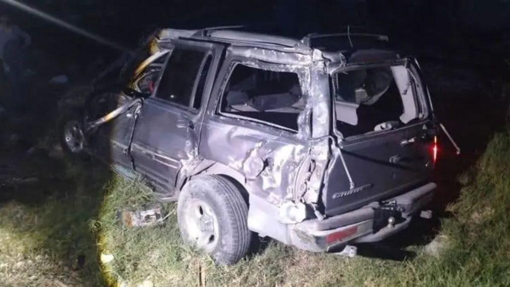 Night time crash scene a dark SUV off the road severely damaged on the left side with a flat front wheel and shattered windows in a grassy area   Informe Regio