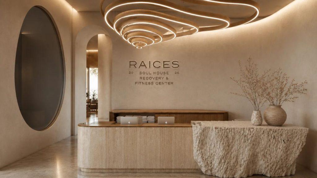Reception area of a chic wellness center with a curved stone front desk and warm beige walls RAICES sign reads Soul House Recovery  Fitness Center   Informe Regio