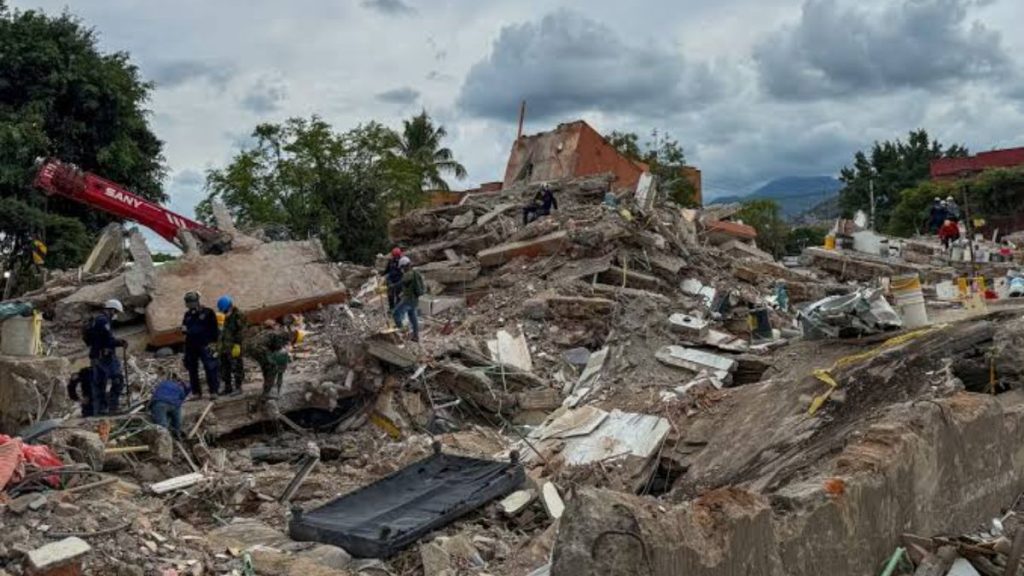 Rescue workers explore a collapsed building amid rubble and debris after a disaster with a red crane in the background and cloudy sky above   Informe Regio