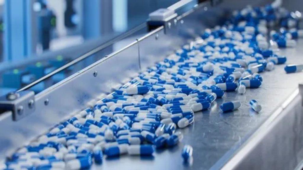 Blue and white capsule pills on a stainless steel conveyor belt in a pharmaceutical facility   Informe Regio