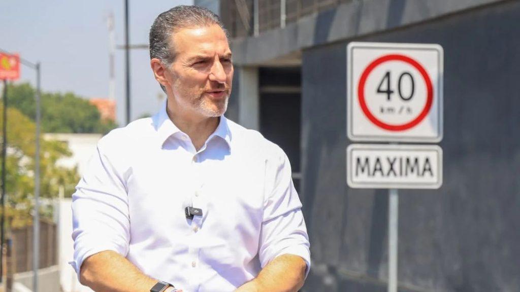 Man in a white shirt with a lapel mic talks outdoors with a 40 kmh speed sign and a MAXIMA sign in the background   Informe Regio
