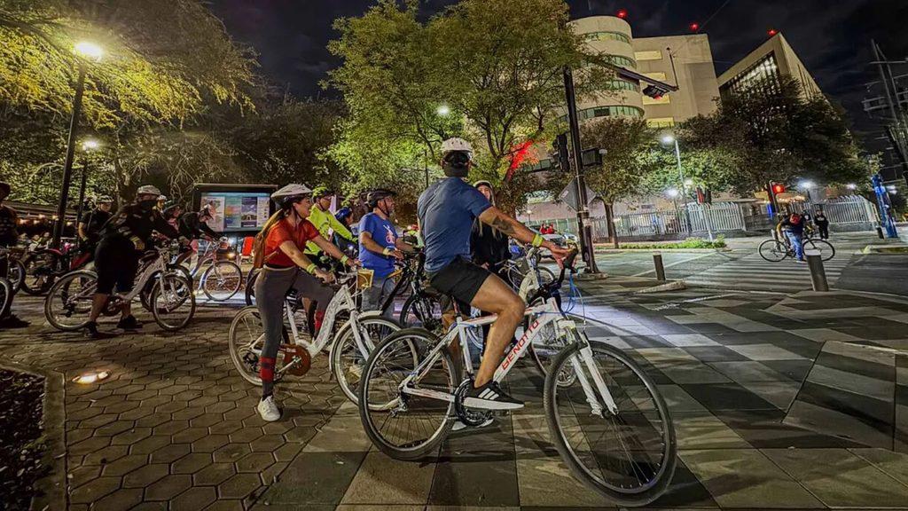 Informe-regio-rodada-policia-san-pedro-segurojpg - Informe Regio Group of cyclists on white bikes gathered at night in a city plaza under streetlights and modern buildings in the background Informe Regio