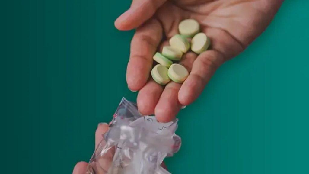 Hands holding several pale green pills above a torn blister pack on a teal background   Informe Regio