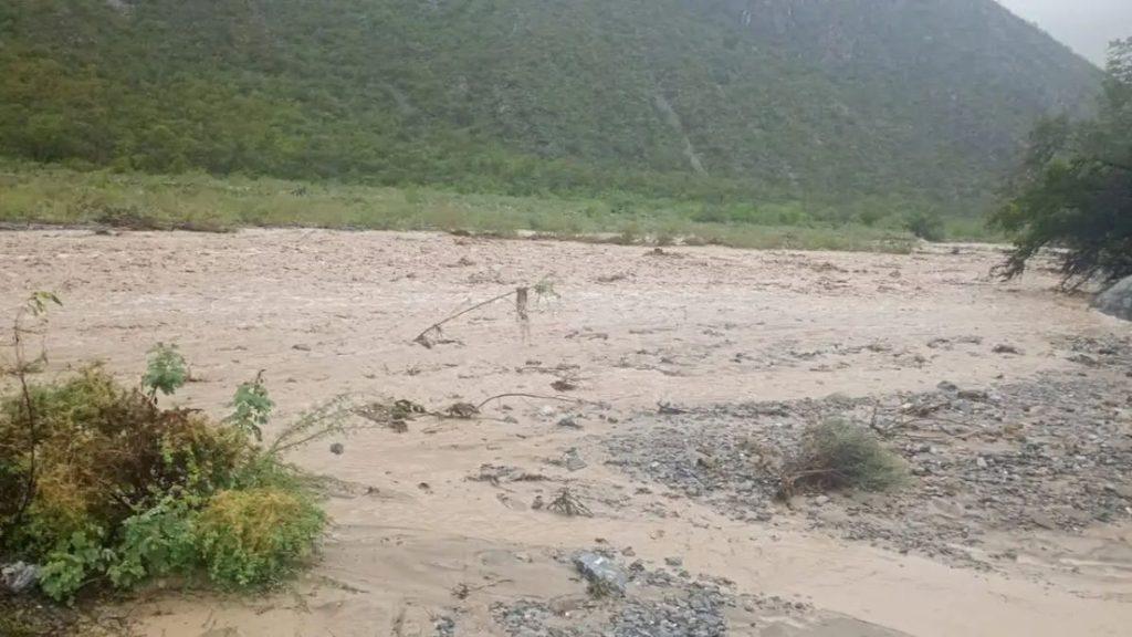 Dry riverbed with mud and scattered rocks green shrubs on the left and forested hills in the background   Informe Regio
