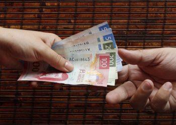 Informe-regio-mexico-salario-minimojpg - Informe Regio Two hands pass a stack of Mexican peso bills from one person to another showing various colorful notes like 100s and 200s in motion Informe Regio