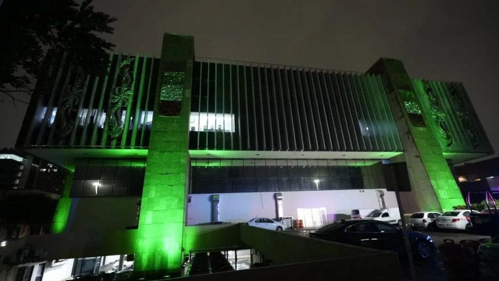 Night view of a modern building lit in green with tall columns and a glass façade cars parked outside   Informe Regio