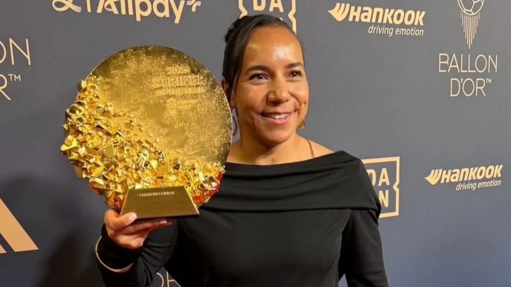 Smiling woman in a black dress holding a large gold circular trophy at an awards event backdrop with sponsor logos   Informe Regio