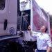 Man in a white shirt stands beside a large white truck with pink branding reaching up to connect a cable to the vehicles equipment outside a building complex at a daytime event   Informe Regio