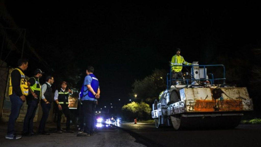 Nighttime highway crew in high visibility vests chat near a large road roller on a dark street roadwork site   Informe Regio