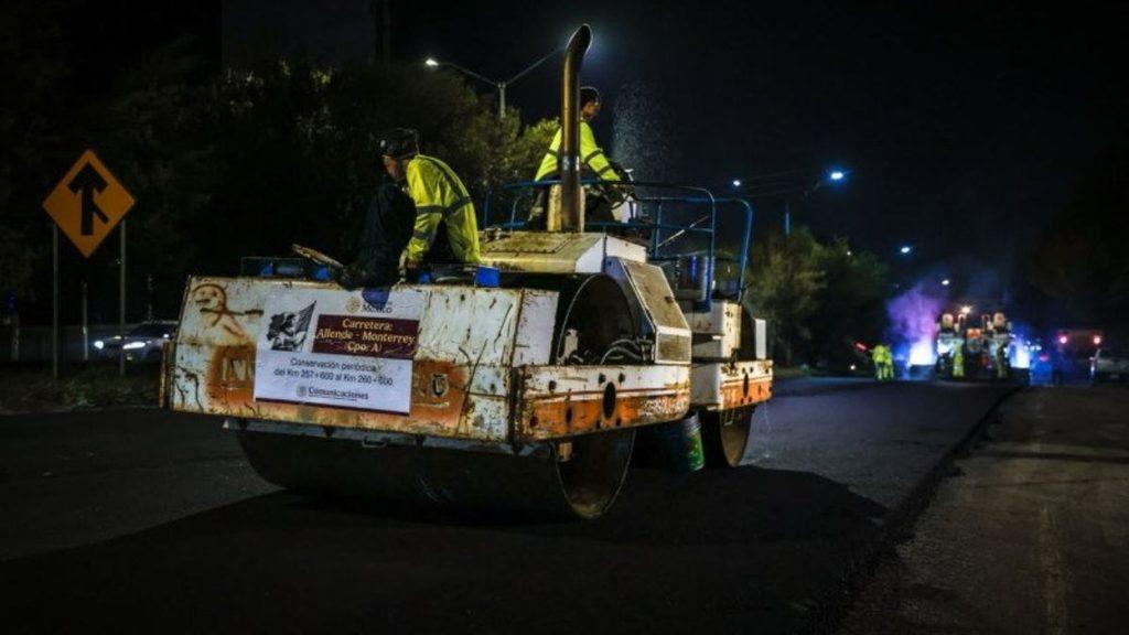 Nighttime road construction with a large asphalt paver and workers in high visibility vests paving a street A warning sign and streetlights are visible in the background   Informe Regio