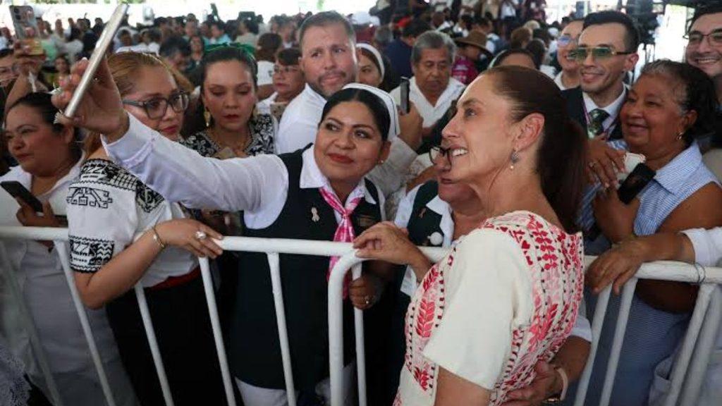 A woman in a white blouse with red embroidery smiles as she takes a selfie with a crowd behind a metal barrier   Informe Regio