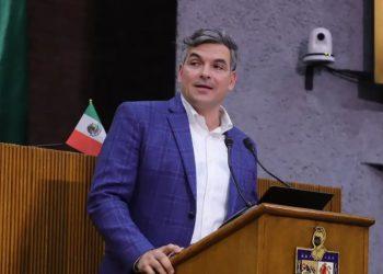 Man in a blue blazer and white shirt speaks at a wooden podium with two microphones a small Mexican flag is visible behind him   Informe Regio
