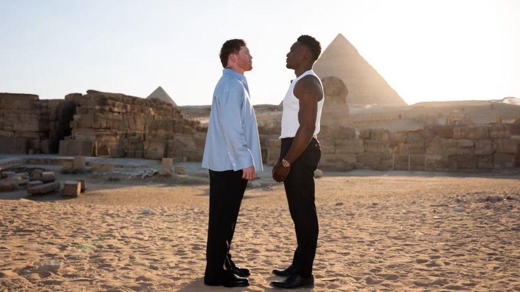 Two men stand chest to chest and face off in a desert with pyramids visible in the background at sunset   Informe Regio