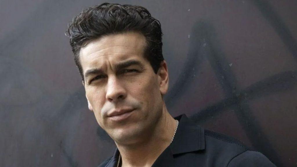 Portrait of a man with slicked back dark hair wearing a black shirt looking slightly to the side against a dark background   Informe Regio