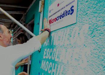 Man in a white shirt presses a sign onto a turquoise wall promoting a microcredit program Microcréditos   Informe Regio